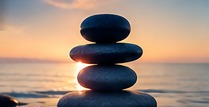 Balanced stones beside calm water at sunset.